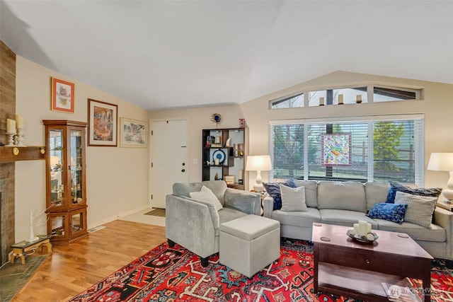 living room with a tiled fireplace, vaulted ceiling, and wood-type flooring