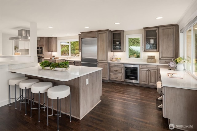 kitchen with a breakfast bar, light countertops, glass insert cabinets, appliances with stainless steel finishes, and beverage cooler