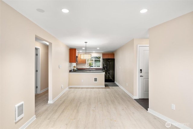 kitchen featuring kitchen peninsula, light hardwood / wood-style flooring, black fridge, and decorative light fixtures