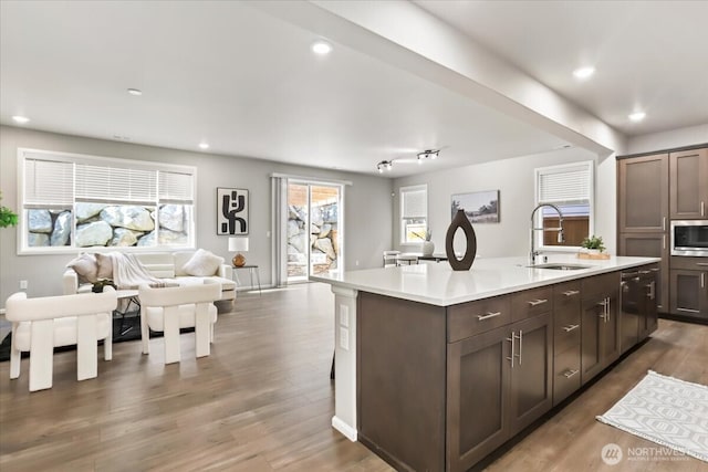 kitchen with dark brown cabinetry, open floor plan, wood finished floors, light countertops, and a sink