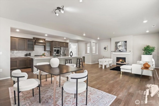 dining area featuring a lit fireplace, dark wood-type flooring, recessed lighting, and baseboards