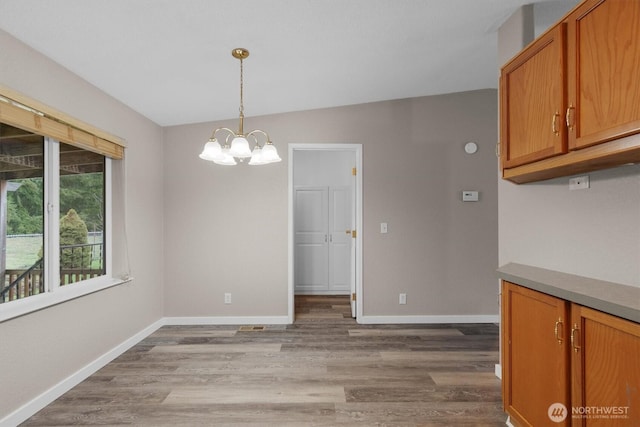 unfurnished dining area featuring a chandelier, wood finished floors, and baseboards