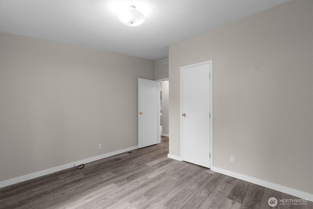 unfurnished room with visible vents, a textured ceiling, baseboards, and wood finished floors