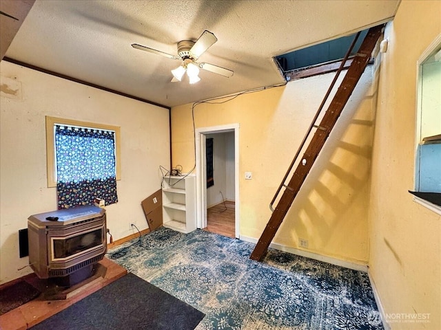 interior space featuring a textured ceiling, a wood stove, and a ceiling fan