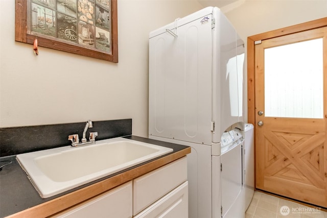 washroom with cabinet space, stacked washing maching and dryer, and a sink