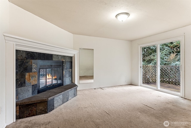 unfurnished living room with carpet flooring, visible vents, a tiled fireplace, and a textured ceiling