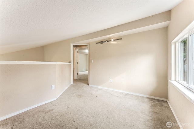 spare room with light carpet, baseboards, vaulted ceiling, and a textured ceiling