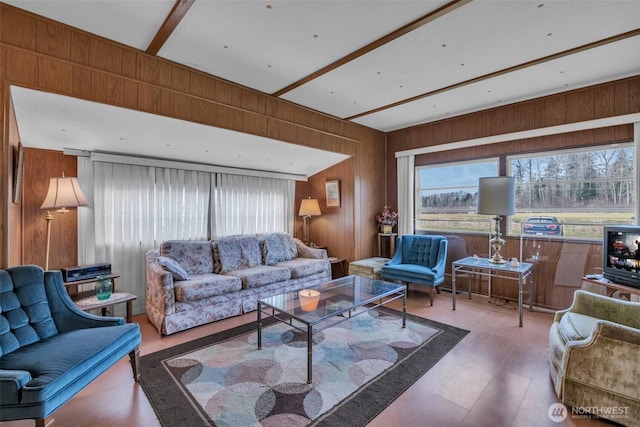 living area with a healthy amount of sunlight, beamed ceiling, and wooden walls