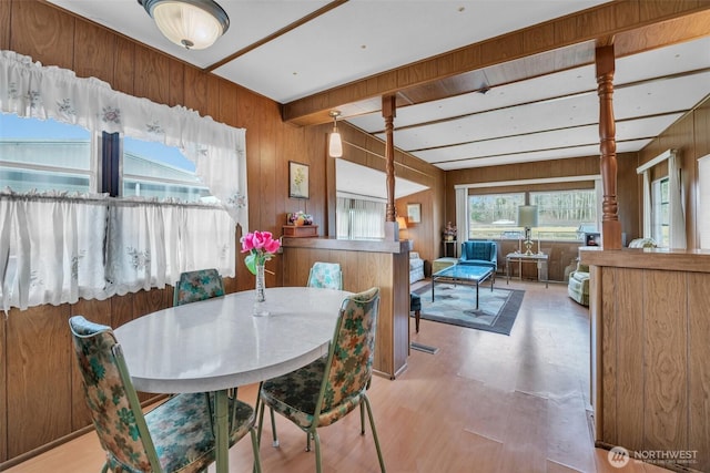 dining area featuring light wood-style flooring, wooden walls, and beamed ceiling