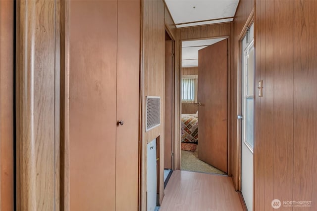 hallway with light wood-style floors, visible vents, and wood walls