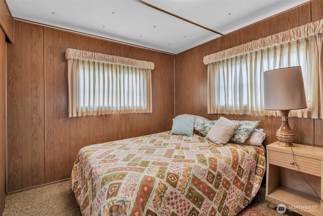 bedroom with carpet floors, multiple windows, and wood walls