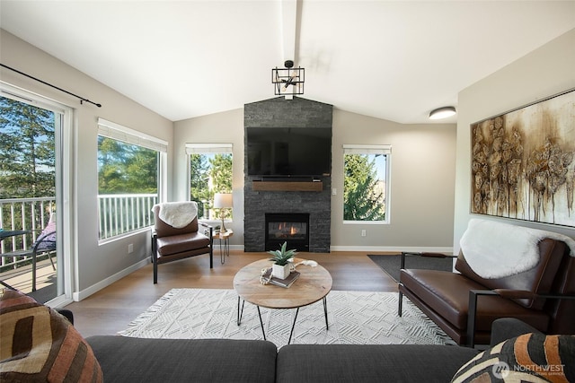 living room featuring vaulted ceiling, a stone fireplace, wood finished floors, and a wealth of natural light