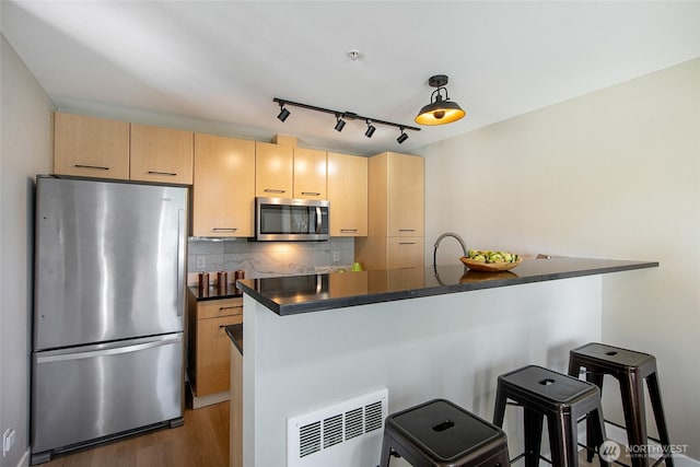 kitchen featuring appliances with stainless steel finishes, dark countertops, light brown cabinets, and tasteful backsplash