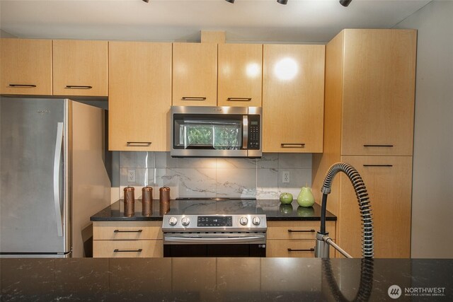 kitchen featuring stainless steel appliances, dark stone countertops, and light brown cabinetry