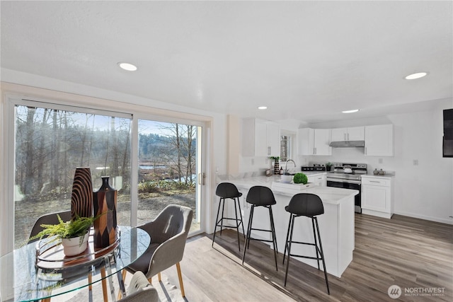 kitchen with a breakfast bar area, stainless steel range with electric stovetop, light wood-type flooring, white cabinetry, and kitchen peninsula