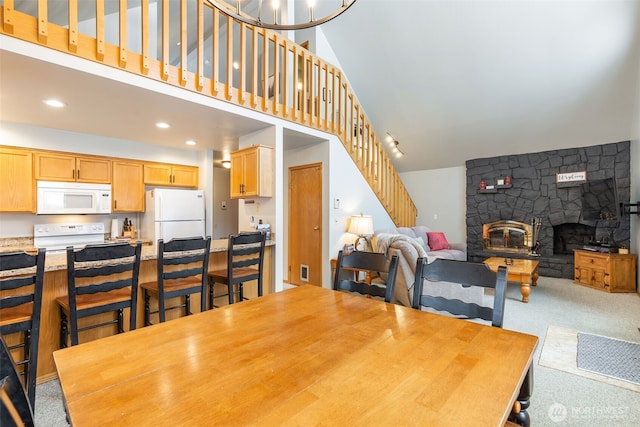 dining space featuring a stone fireplace, recessed lighting, light carpet, a high ceiling, and stairs