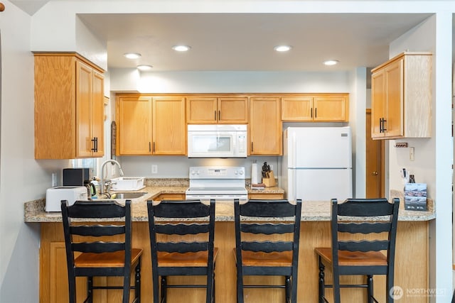 kitchen featuring light stone counters, white appliances, a sink, and a kitchen bar