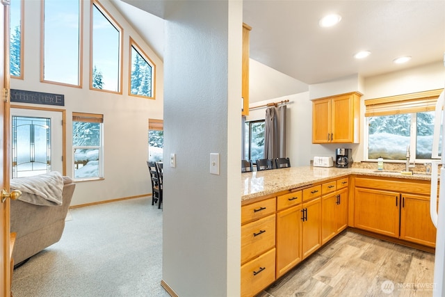 kitchen with plenty of natural light, a peninsula, a sink, and light stone countertops