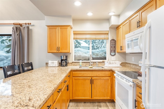 kitchen featuring white appliances, light stone counters, a breakfast bar, a peninsula, and a sink