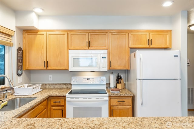 kitchen with light stone counters, white appliances, visible vents, and a sink