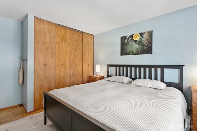 bedroom with a closet, baseboards, a textured ceiling, and light wood finished floors