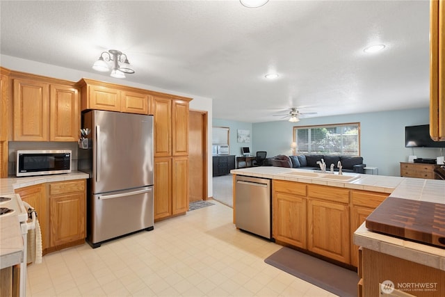 kitchen featuring tile counters, appliances with stainless steel finishes, open floor plan, a sink, and ceiling fan