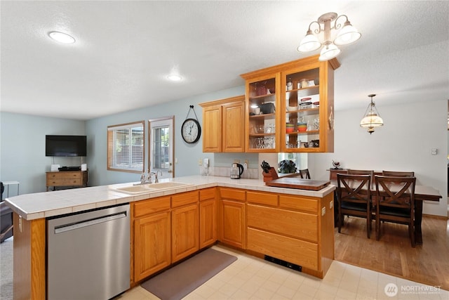 kitchen featuring a peninsula, a sink, hanging light fixtures, dishwasher, and brown cabinetry