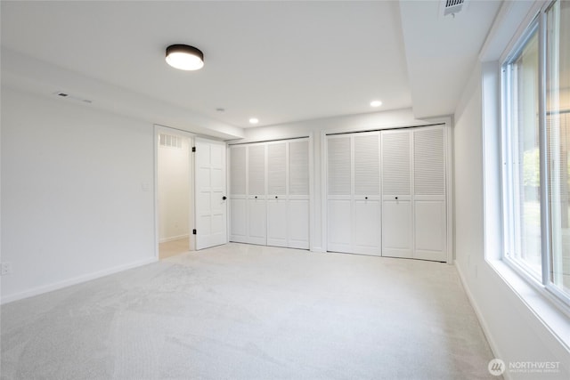 unfurnished bedroom with light carpet and multiple closets