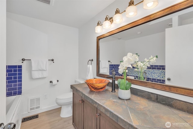 full bath featuring toilet, vanity, wood finished floors, and visible vents