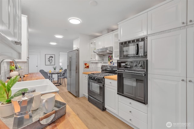 kitchen with light wood finished floors, butcher block countertops, under cabinet range hood, black appliances, and white cabinetry