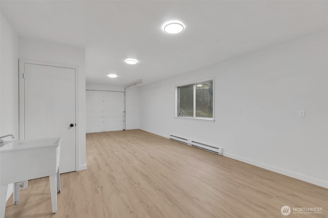 unfurnished room featuring baseboard heating, light wood-type flooring, a sink, and baseboards