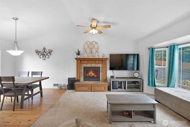 living area featuring a fireplace, lofted ceiling, visible vents, a ceiling fan, and wood finished floors