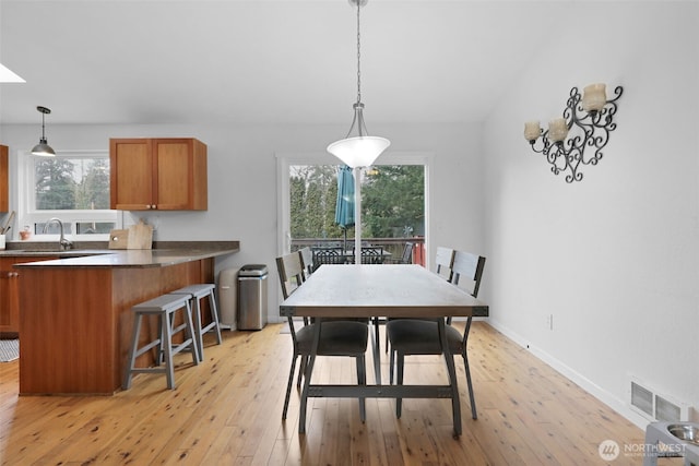 dining space featuring light wood-type flooring, visible vents, vaulted ceiling with skylight, and baseboards