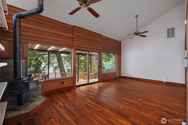 unfurnished living room featuring high vaulted ceiling, a wood stove, visible vents, and wood finished floors