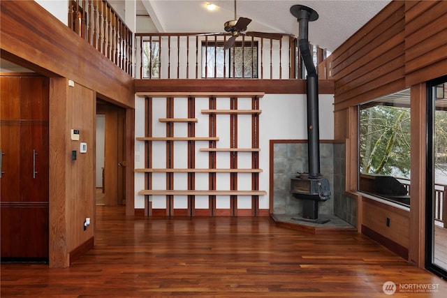 unfurnished living room featuring dark wood-style floors, a towering ceiling, and a wood stove