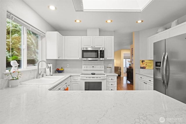 kitchen with appliances with stainless steel finishes, sink, dark wood-type flooring, white cabinets, and light stone countertops