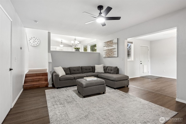 living area with baseboards, ceiling fan with notable chandelier, dark wood-type flooring, and stairway