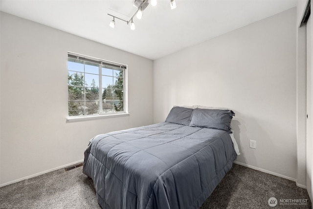 bedroom with dark colored carpet, rail lighting, baseboards, and visible vents