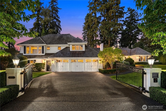 shingle-style home with driveway, a lawn, a fenced front yard, an attached garage, and a gate