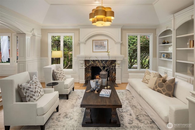 living area with built in features, a wainscoted wall, ornamental molding, a decorative wall, and a high end fireplace