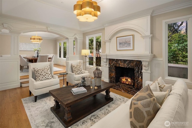 sitting room featuring arched walkways, a wainscoted wall, a notable chandelier, decorative columns, and wood finished floors