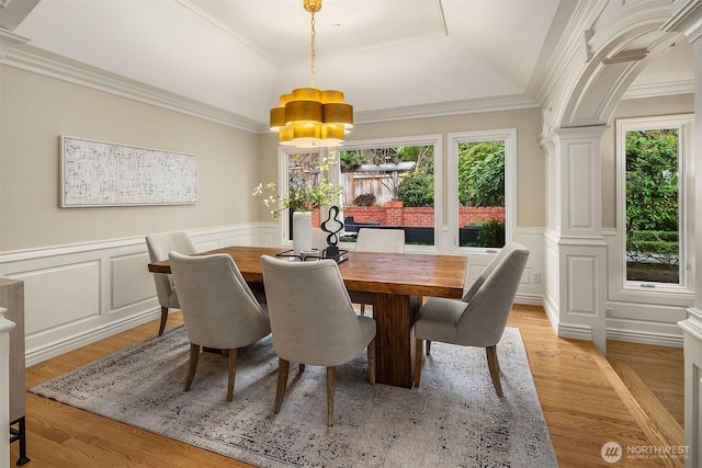 dining room with a healthy amount of sunlight, light wood-style flooring, crown molding, and wainscoting