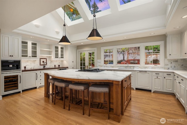 kitchen featuring beverage cooler, stainless steel gas cooktop, a skylight, a kitchen island, and a raised ceiling