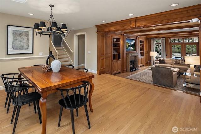 dining area with light wood finished floors, a fireplace with flush hearth, stairs, a notable chandelier, and recessed lighting