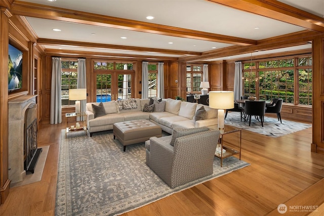 living room featuring french doors, light wood finished floors, a decorative wall, a premium fireplace, and beamed ceiling