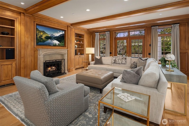 living room with light wood-type flooring, a warm lit fireplace, built in shelves, and beamed ceiling