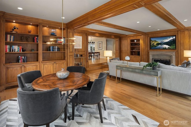 dining space featuring wooden walls, a fireplace, built in features, light wood finished floors, and beamed ceiling