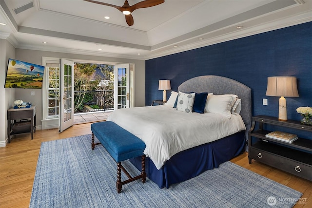 bedroom featuring a raised ceiling, an accent wall, wood finished floors, access to outside, and crown molding