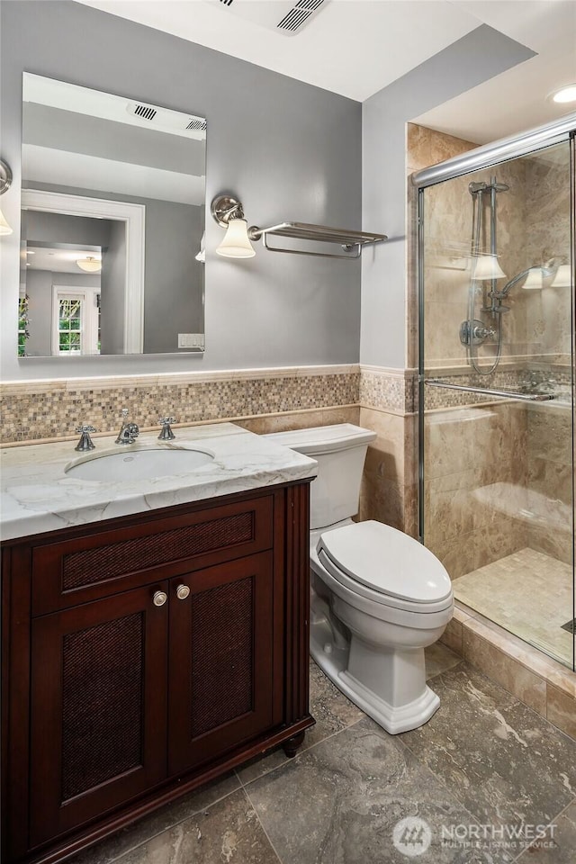 full bathroom with toilet, vanity, tile walls, wainscoting, and a shower stall