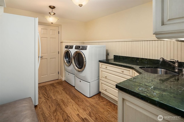 clothes washing area featuring wainscoting, wood finished floors, a sink, and washing machine and clothes dryer